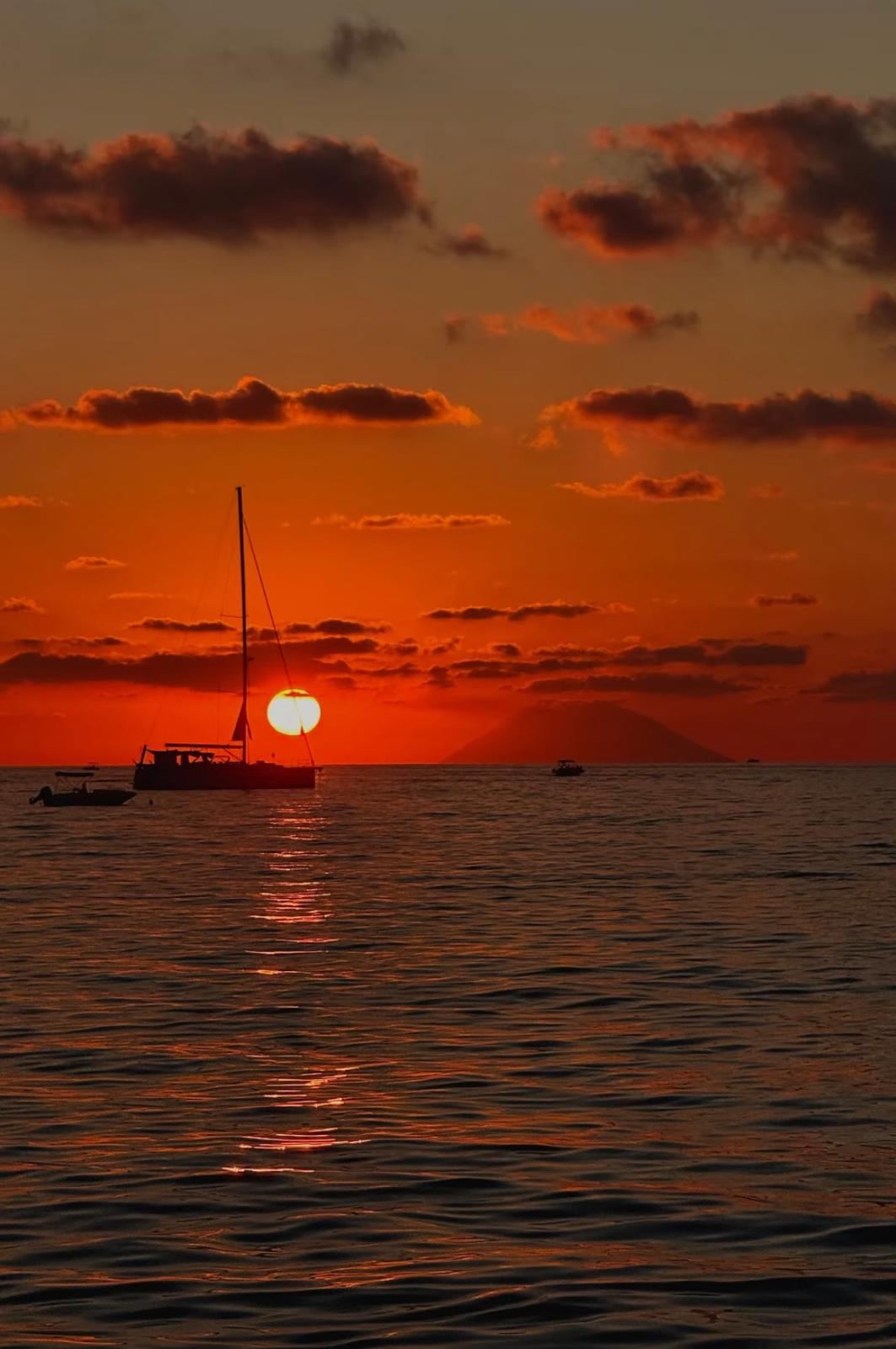 Il sole che tramonta sul mare con una barca a vela all'orizzonte