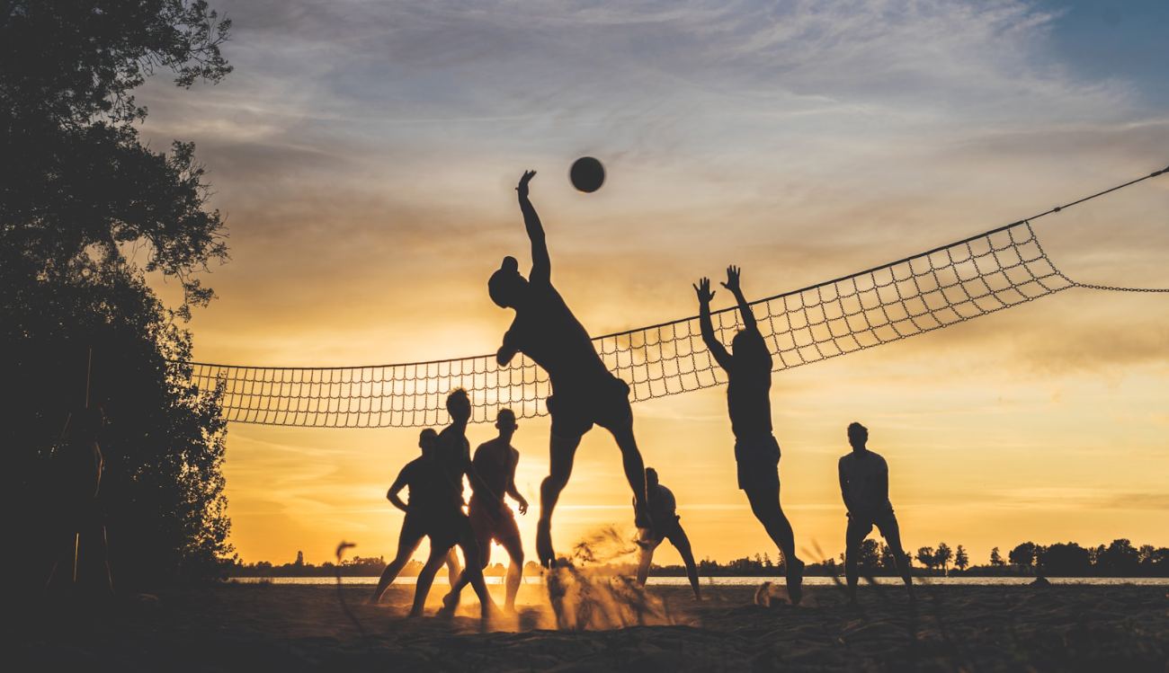 Ragazzi che giocano a beach volley in spiaggia al tramonto